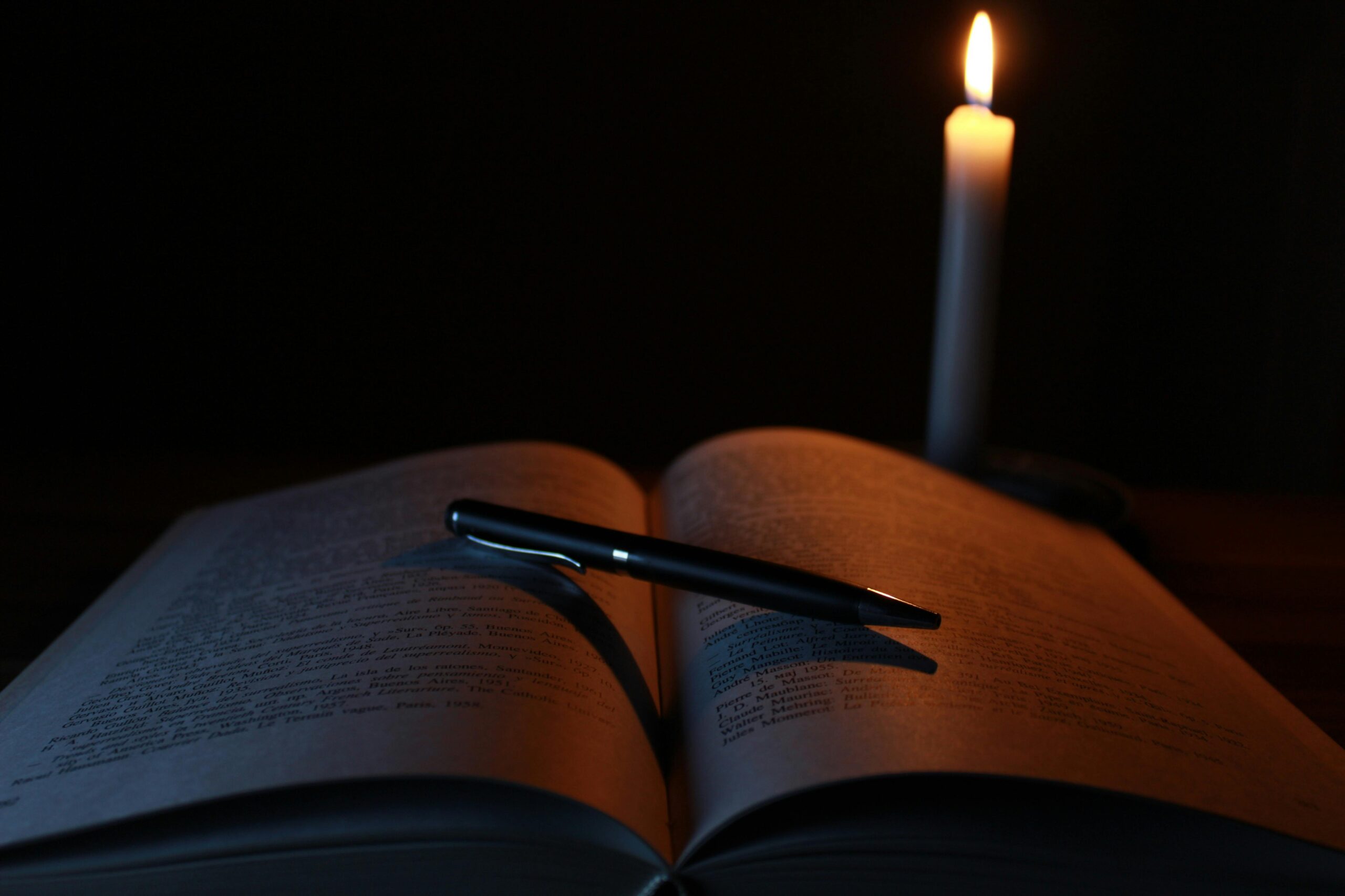 pexels-photo-207700-207700 An open book and pen on a desk illuminated by candlelight, creating a tranquil study atmosphere.